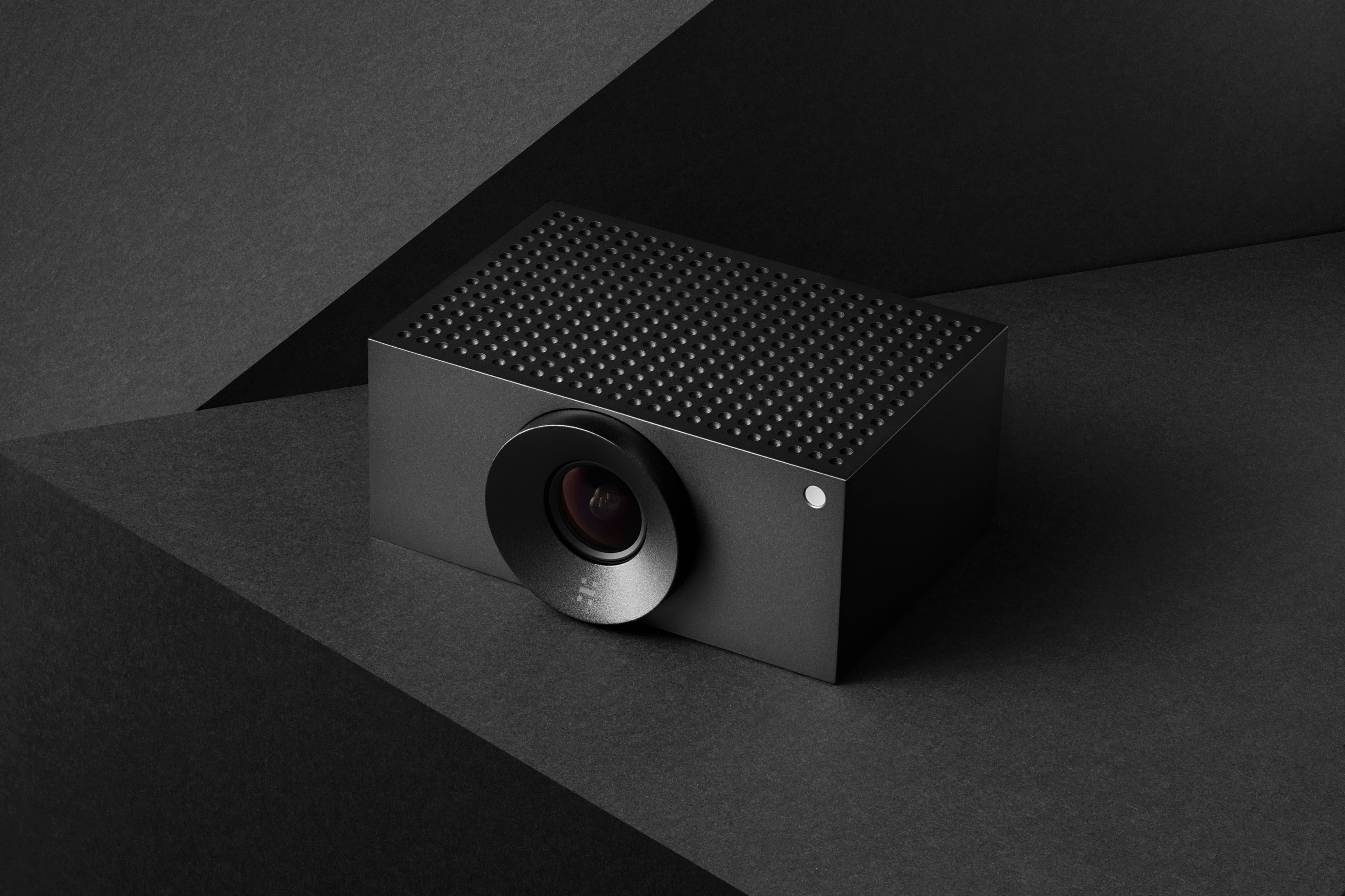 Huddly L1 conference camera, matte black aluminium body with perforated top and front lens, angled view on a dark background